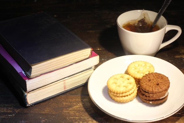 tasse de thé avec petite cuillère, biscuit sur une assiette et une pile de livres sur la table mise au point sélective