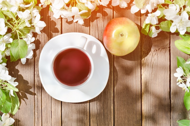 Tasse de thé et pomme mûre parmi pomme fleur sur une table en bois.