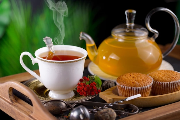 Une tasse de thé avec une théière et des muffins sur une table