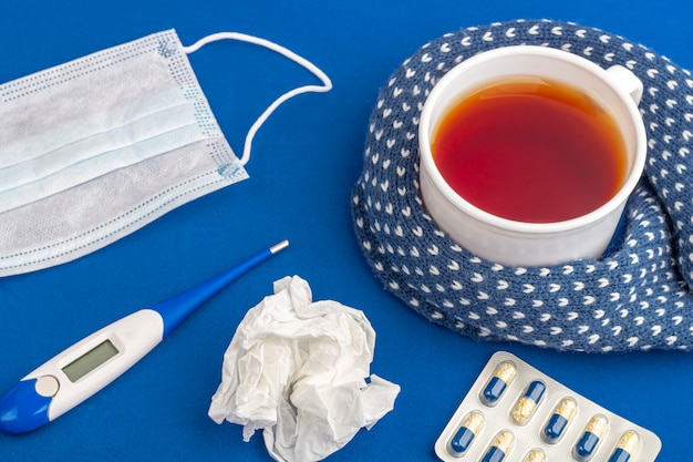 Tasse de thé, thermomètre, serviette froissée et masque médical sur bleu