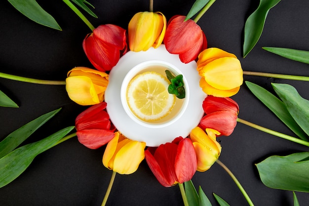 Tasse de thé avec des tulipes rouges et jaunes autour.