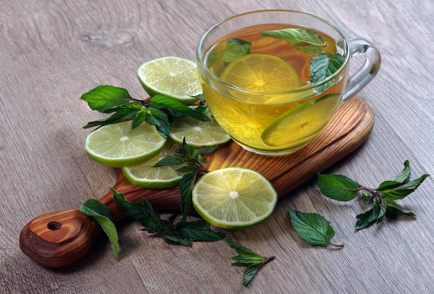 une tasse de thé en verre avec des feuilles de citron et de menthe.