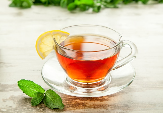 Tasse de thé en verre sur une table en bois avec des feuilles de citron et de menthe.