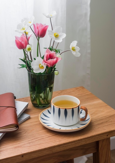 Une tasse de thé vert un bouquet de fleurs printanières un carnet sur une table en bois dans un salon cosy Slow tea party