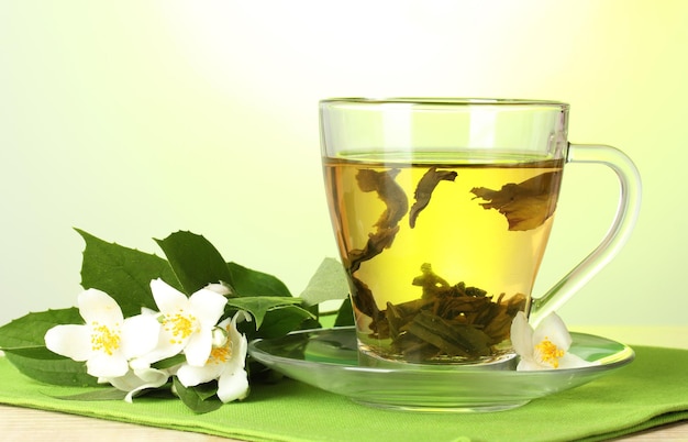 Une tasse de thé vert avec des fleurs de jasmin sur une table en bois sur un fond vert