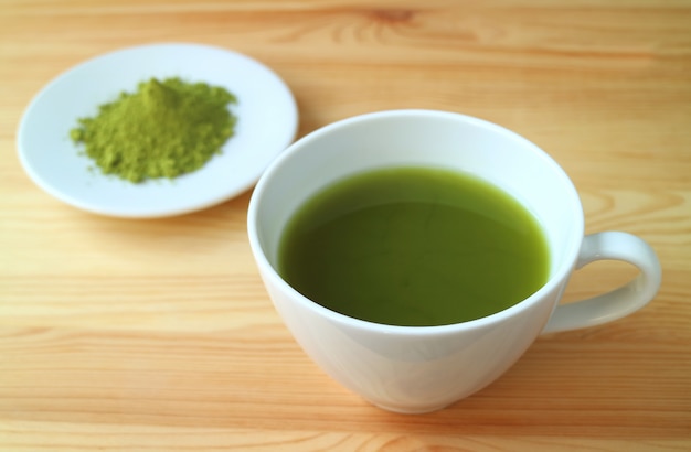 Une tasse de thé vert Matcha chaud aux couleurs vives avec de la poudre de thé Matcha floue en arrière-plan