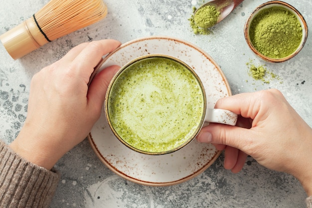 Tasse de thé vert Matcha dans les mains de la femme.