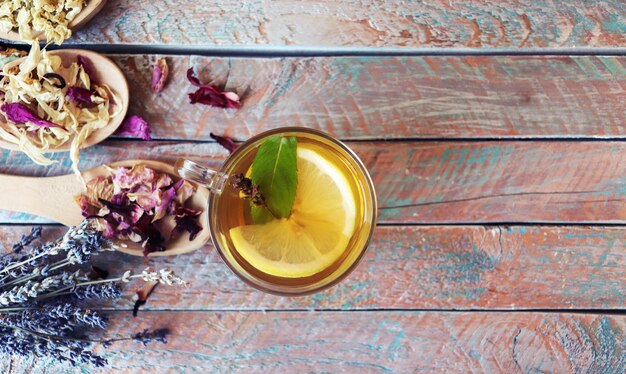 Tasse de thé vert à la menthe et aux pétales secs de citron de plantes utiles sur une bannière de table en bois