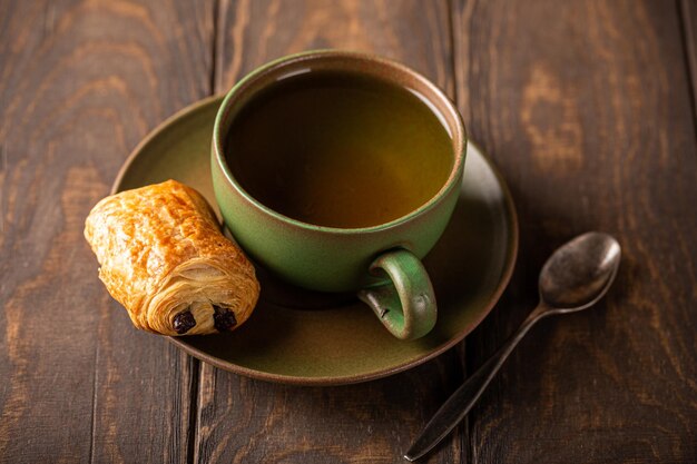 Une tasse de thé vert avec un mini-pain au chocolat.