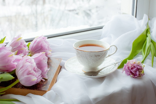 Tasse de thé un vieux livre un bouquet de tulipes sur la fenêtre