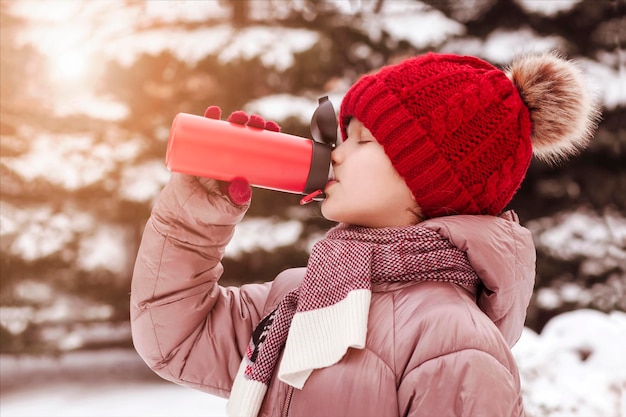 Tasse thermos pour enfants en hiver. Fille enfant ado boire du thé chaud dans une tasse thermos en marche d'hiver