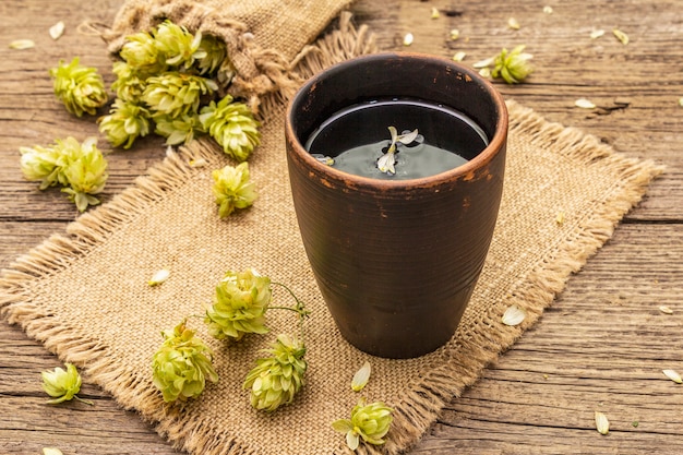 Tasse de tisane apaisante avec du houblon sauvage frais. Cônes de houblon en sac sur planches vintage