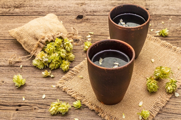 Tasse de tisane apaisante avec du houblon sauvage frais. Cônes de houblon en sac sur planches vintage