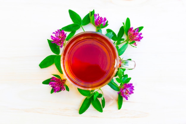 La tasse de tisane noire avec des fleurs de trèfle rouge sur table en bois