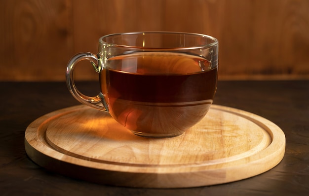 Tasse transparente avec du thé noir sur un plateau en bois