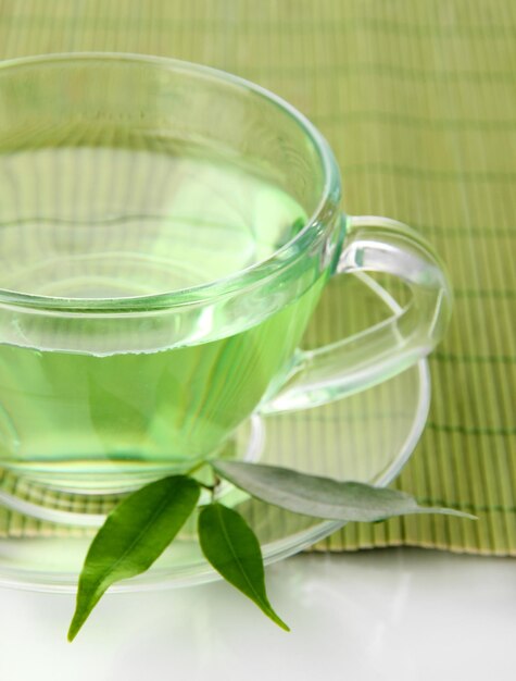 Tasse transparente de thé vert sur tapis de bambou isolé sur blanc