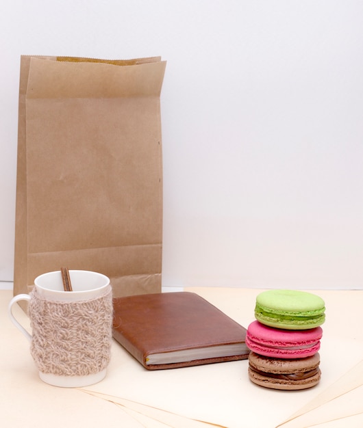 Tasse tricotée, macarons colorés et bloc-notes sur un sac en papier