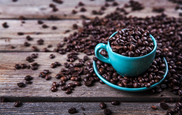 Tasse turquoise avec des grains de café sur un bois.