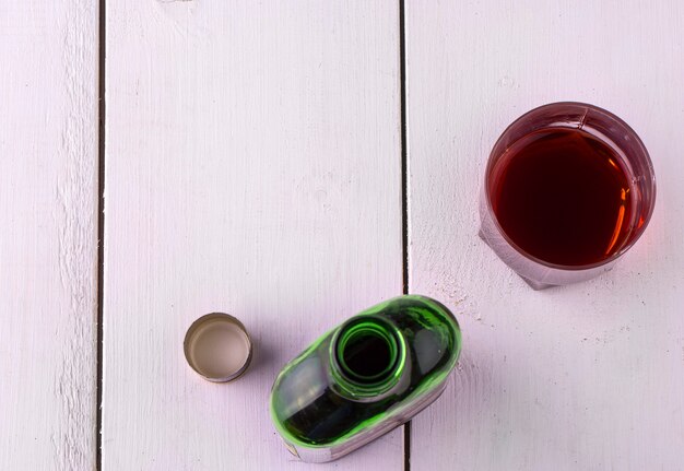 Tasse en verre avec de l'alcool et ouvrez une bouteille de whisky sur une table en bois blanche. Vue d'en-haut