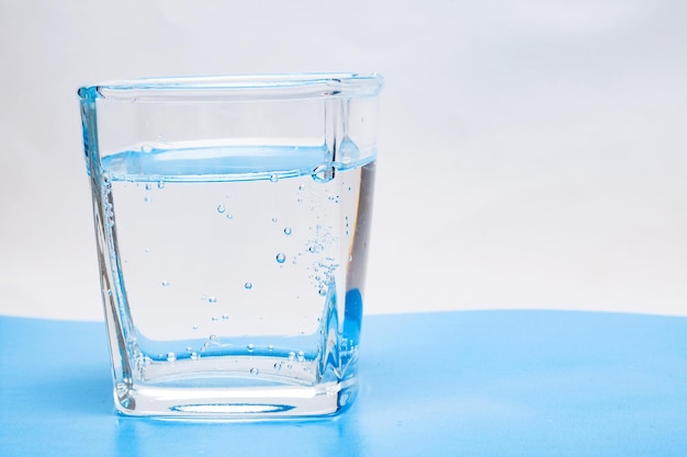 Tasse en verre avec de l'eau avec des bulles sur un fond blanc