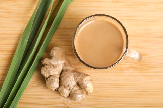 Tasse en verre de thé au gingembre chaud avec rhizome de gingembre (racine) en tranches isolé sur une surface en bois