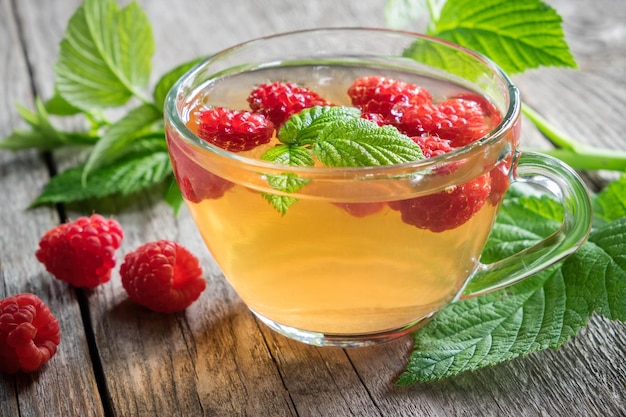 Tasse en verre de thé aux fruits avec des framboises sur planche de bois