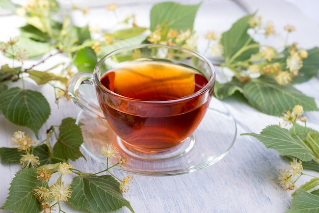 Tasse en verre de thé de tilleul et de fleurs de tilleul sur une table en bois blanc. Boisson chaude de soins de santé.