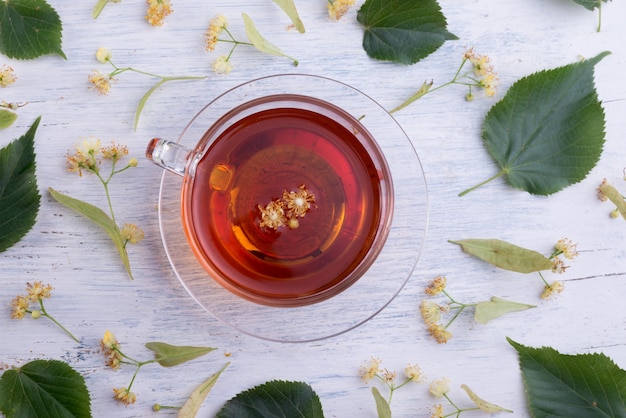 Tasse en verre de thé de tilleul et de fleurs de tilleul sur une vue de dessus de table en bois blanc. Boisson chaude de soins de santé.