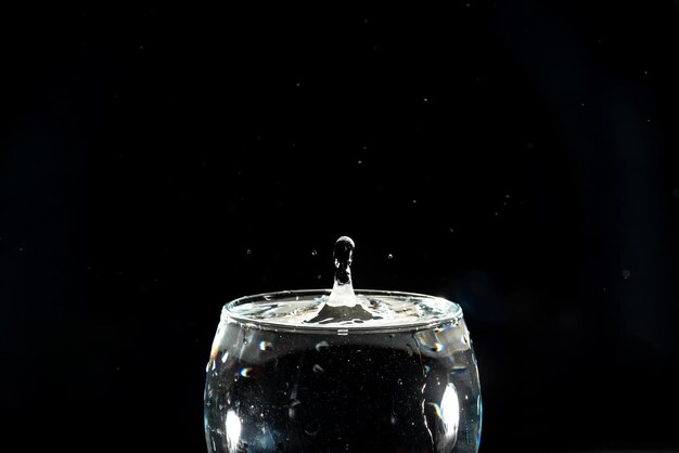 Une tasse de verre transparente avec de l'eau à l'intérieur et une goutte éclaboussant vers le haut