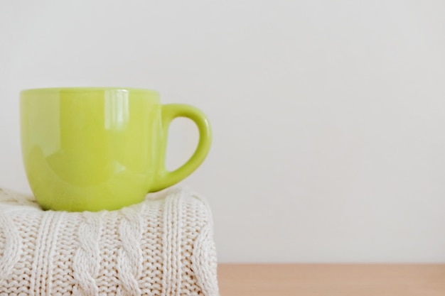 Une tasse verte avec une boisson chaude café sur une pile de chandails tricotés soigneusement pliés fond beige