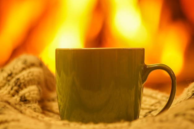 Tasse verte pour le thé ou le café et les choses en laine près de la cheminée