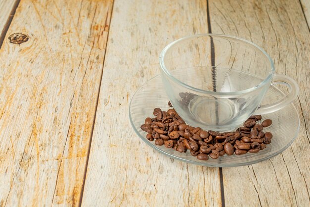 tasse vide en verre transparent, avec des grains de café sur une table en bois