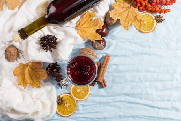 Une tasse de vin chaud avec des épices, une bouteille, des feuilles sèches et des oranges sur la table. Humeur d'automne, méthode pour rester au chaud dans le froid, fond, lumière du matin.