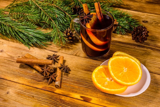 Tasse de vin chaud avec des tranches de cannelle orange et branches de sapin sur table en bois