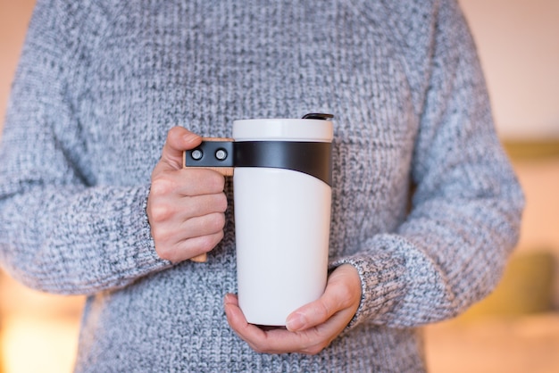 Tasse de voyage Thermos, gobelet blanc, flacon pour thé ou café dans les mains de la femme