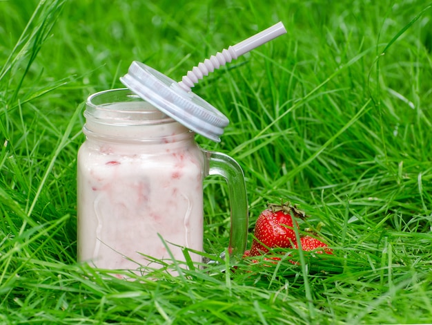 Tasse de yaourt et fraise sur fond d'herbe verte, espace pour le texte