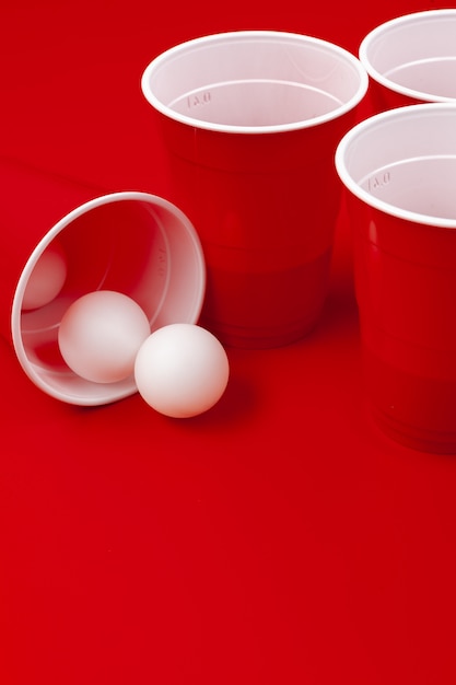 Tasses et boule en plastique sur fond rouge. Jeu de Beer Pong