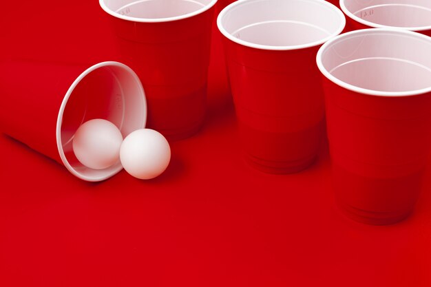 Tasses et boule en plastique sur surface rouge. Jeu de Beer Pong