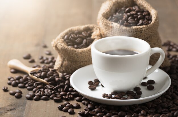 Tasses de café chaud avec de la fumée et des grains de café sur le vieux fond en bois