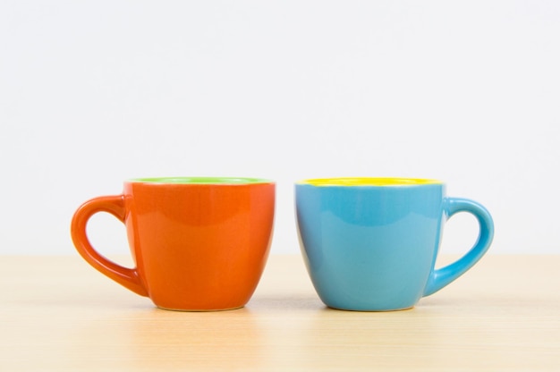 Tasses à café colorées sur planche de bois et fond blanc
