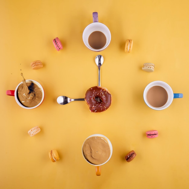 Des tasses de café disposées comme des chiffres dans une horloge au milieu un beignet et des cuillères comme des aiguilles d'horloge