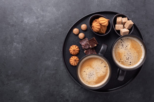 Tasses de café, divers bonbons et épices sur plaque en céramique.