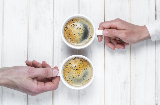 Tasses de café entre les mains de deux personnes. Vue de dessus