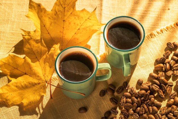 Tasses de café et de grains de café et feuilles jaunes illuminées par la lumière du soleil, jour d'automne.