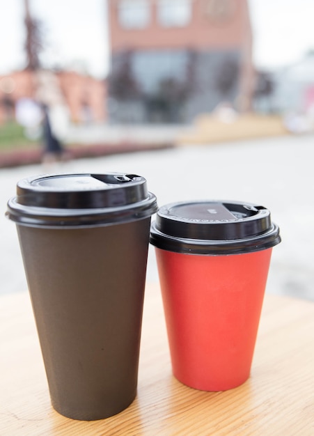 Tasses de café en papier noir et rouge à emporter sur une table en bois à l'extérieur du café. Petit-déjeuner matinal à l'antenne