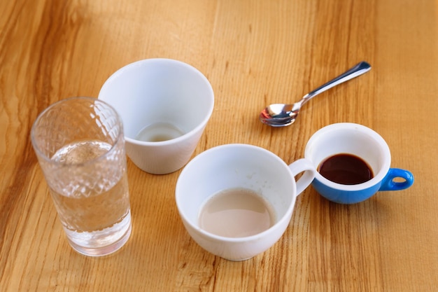 Des tasses à café sales cappuccino et un verre d'eau se tiennent sur une table en bois