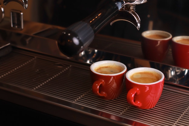 Les tasses à café se tiennent à l'intérieur de la machine à café sur une grille, du café frais est versé à l'intérieur des tasses