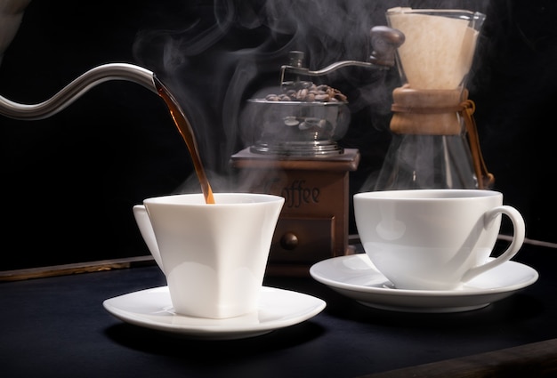Tasses à café à vapeur avec moulin à café, beens et bouilloire sur fond sombre de table en bois grunge
