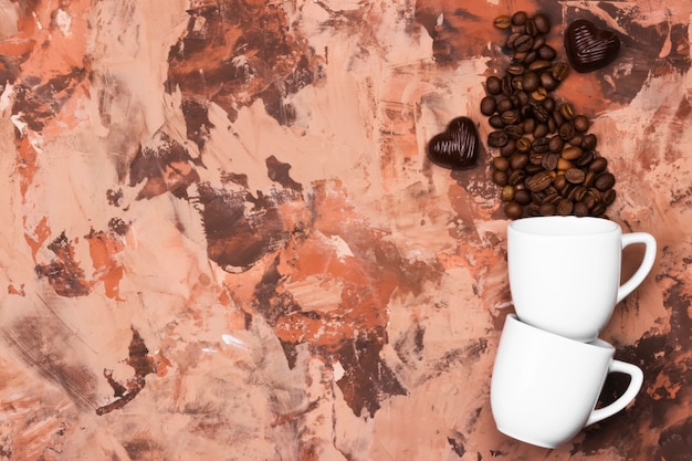 Photo tasses à espresso blanches remplies de grains de café et de chocolat en forme de coeur sur fond marron. vue de dessus, espace copie. contexte alimentaire.