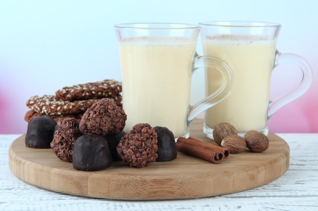 Tasses de lait de poule avec des bonbons et des épices sur table sur fond clair